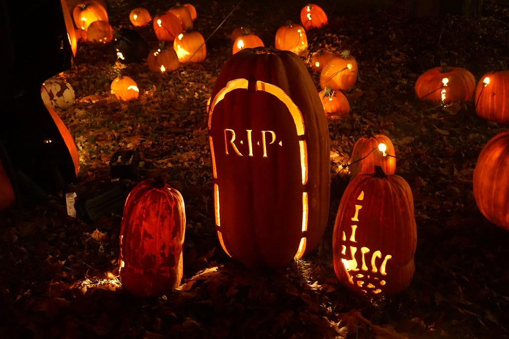 Three carved pumpkings, lit up at night. The middle one says RIP.