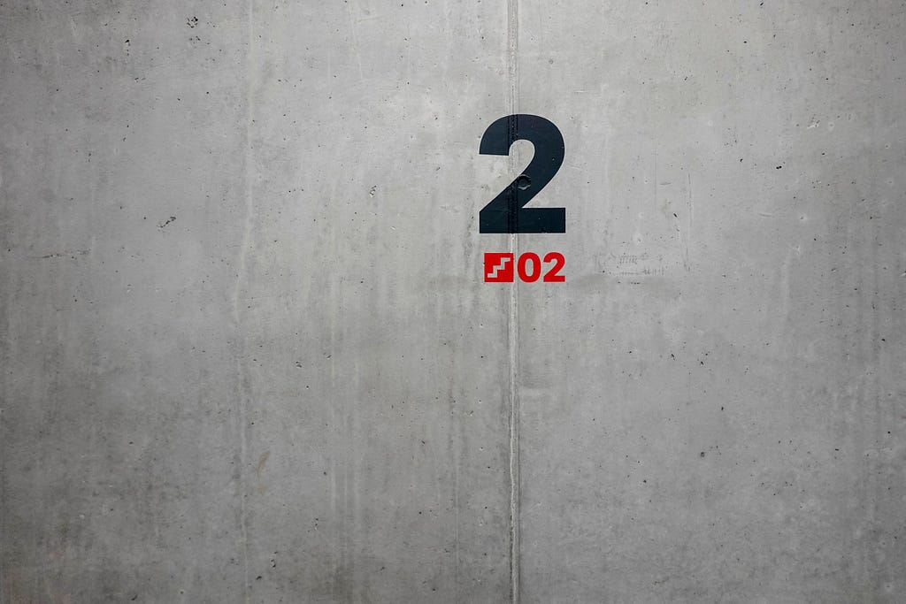 The number 2 in black large type and smaller red type on a grey textured background.