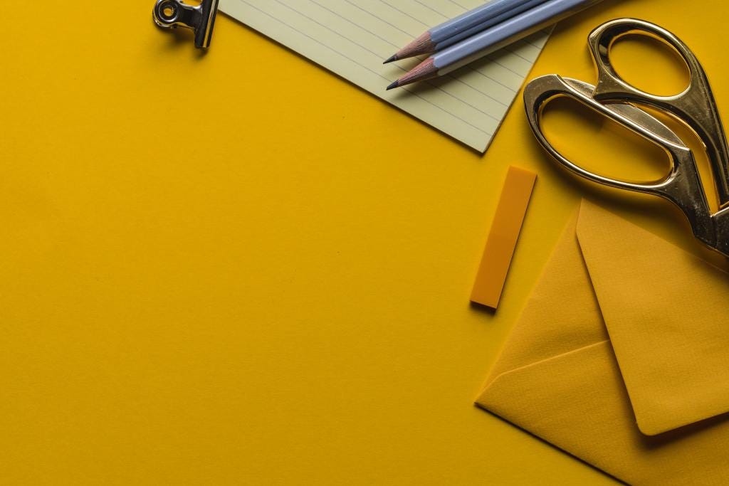 Scissors, envelope, notepad and pencils on gold yellow background.