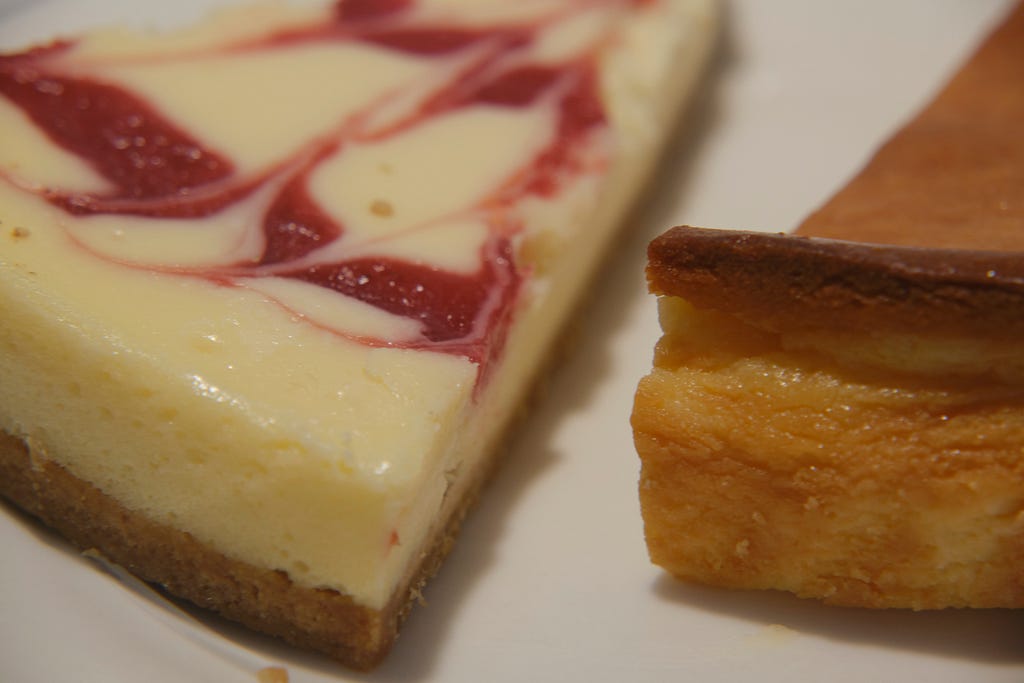 close up of a slice of cheesecake with raspberry swirls next to a slice of plain cheesecake