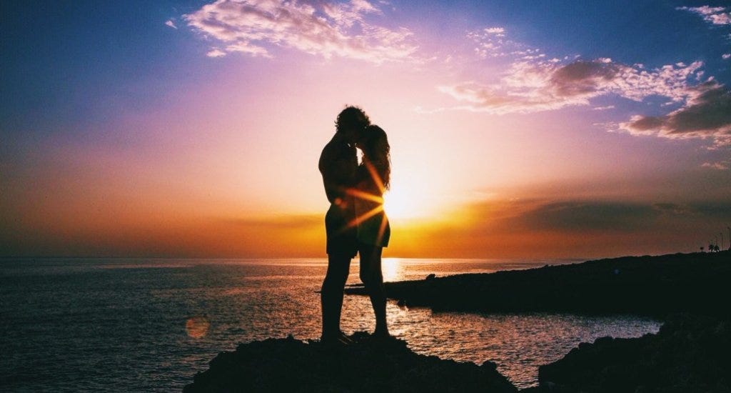 A man and a woman embracing near an ocean during a sunset
