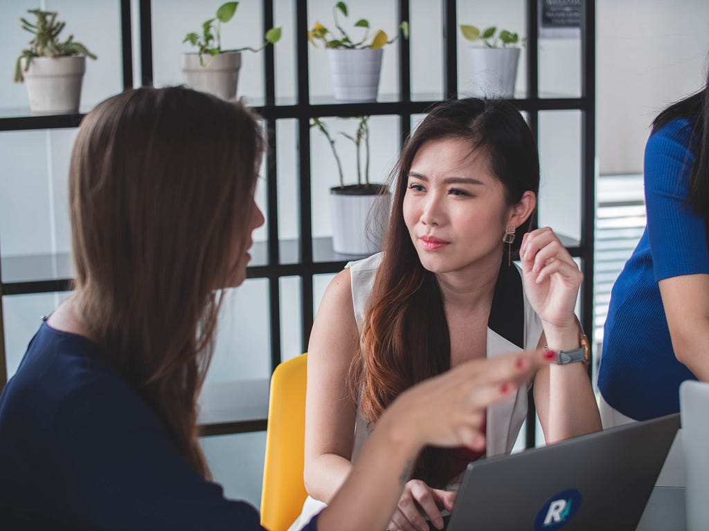 Two seated females speaking with each other