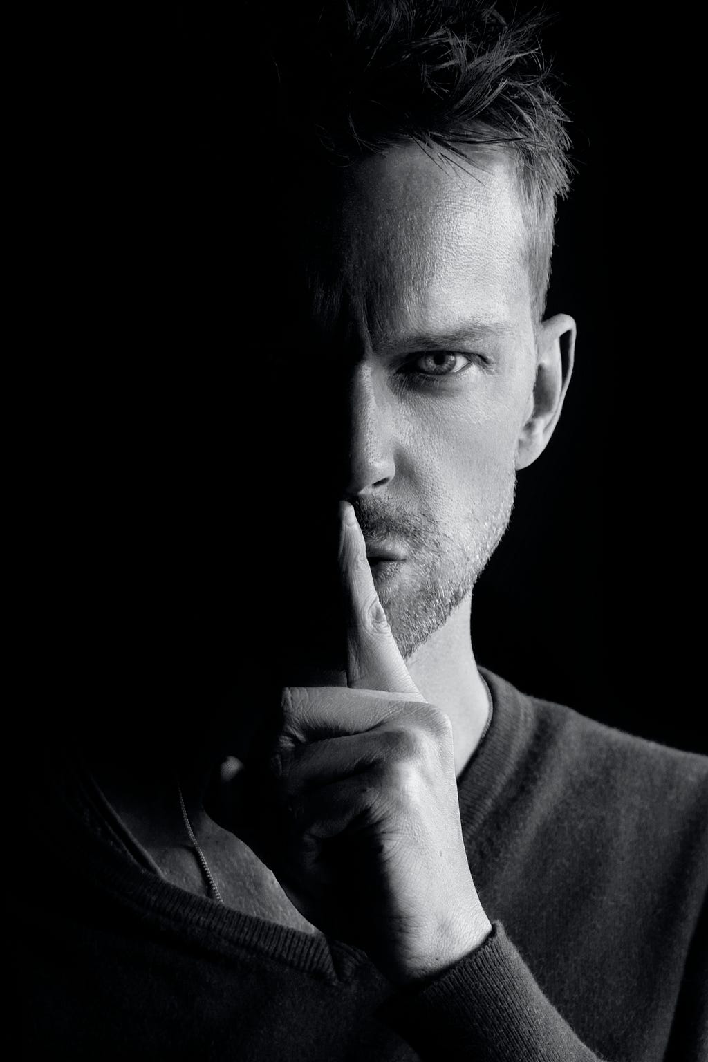 Half-hidden face of a man with his finger over his lips.