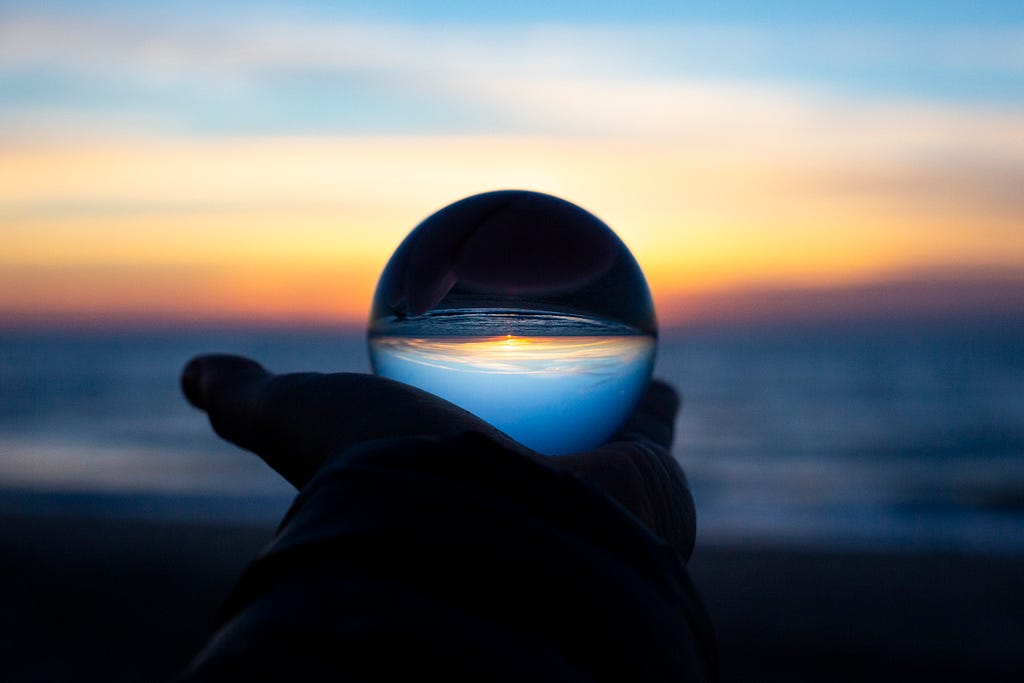 a hand holding a glass ball in front of the ocean