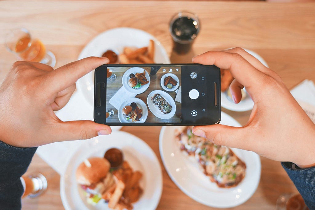 A person taking an aesthetic photo or video of plates of food for social media