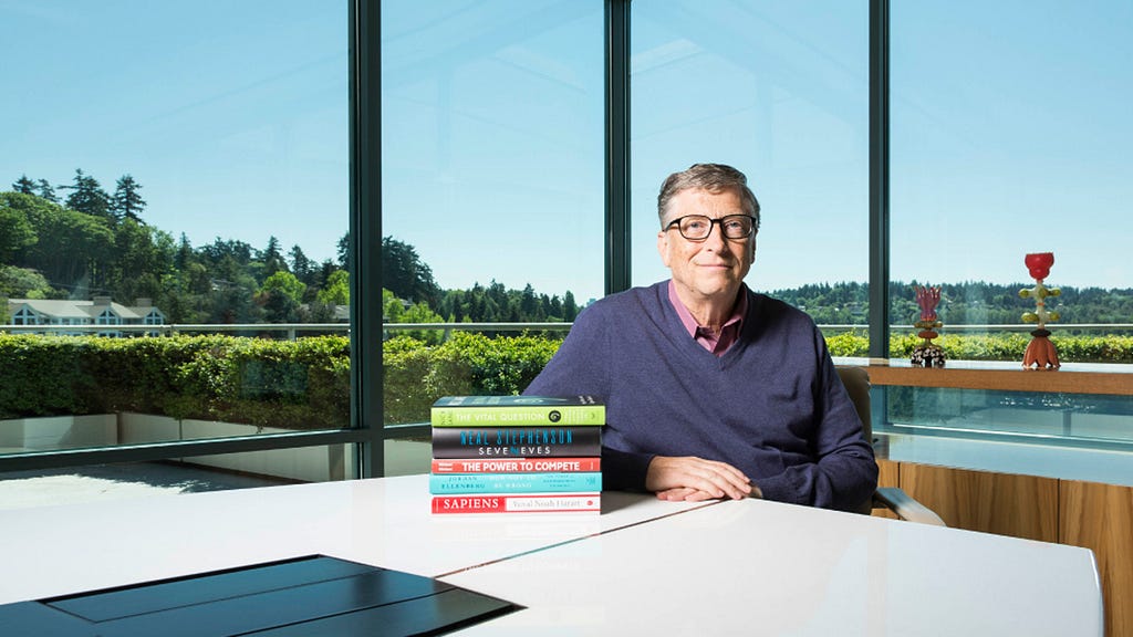Bill gates sitting down with a stack of books.