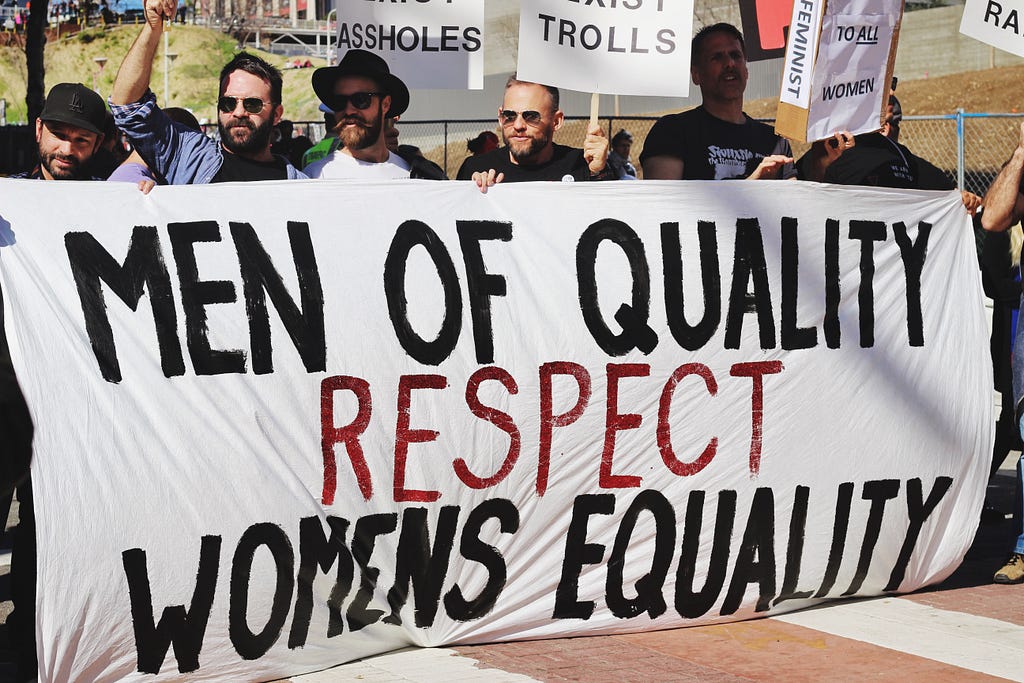 photo of men holding a banner in support of womens equality in article by Sav May about the ERA and Michele Thorne’s activism