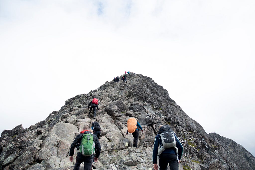 A steep mountain with hikers climbing towards the top.