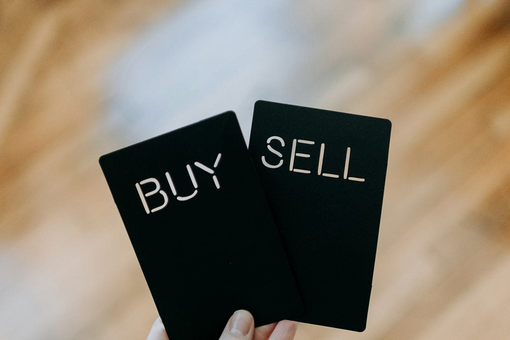A hand holding two cards reading ‘Buy’ and ‘Sell’