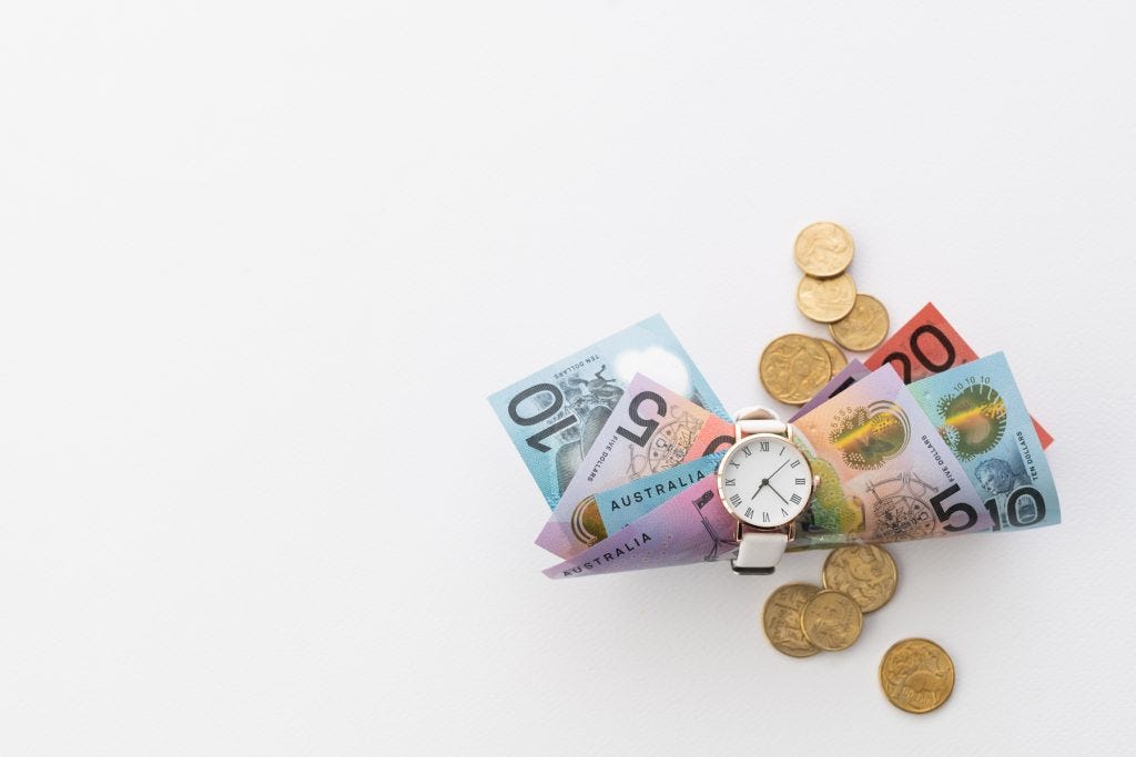 A bunch of Australian currency (notes) stuffed inside the band of a white watch, with gold coins scattered about.