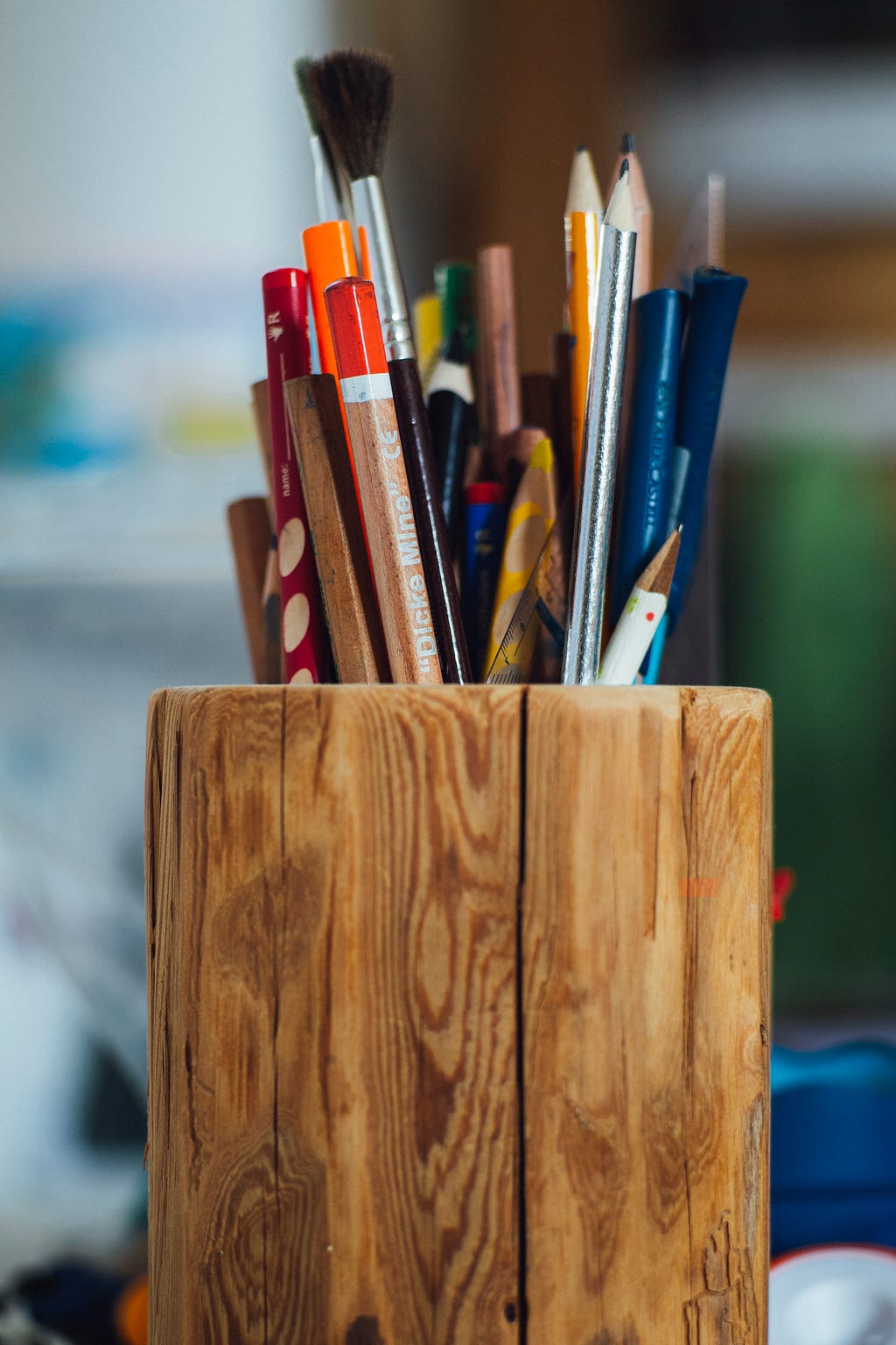 A brown, woody pencil holder filled with colourful pencils.