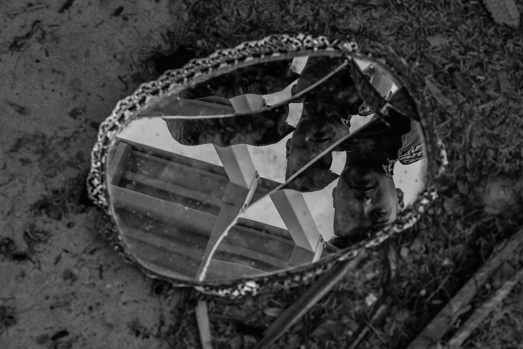 A monochrome photo of a broken mirror on the ground. A man’s face is reflected in it.
