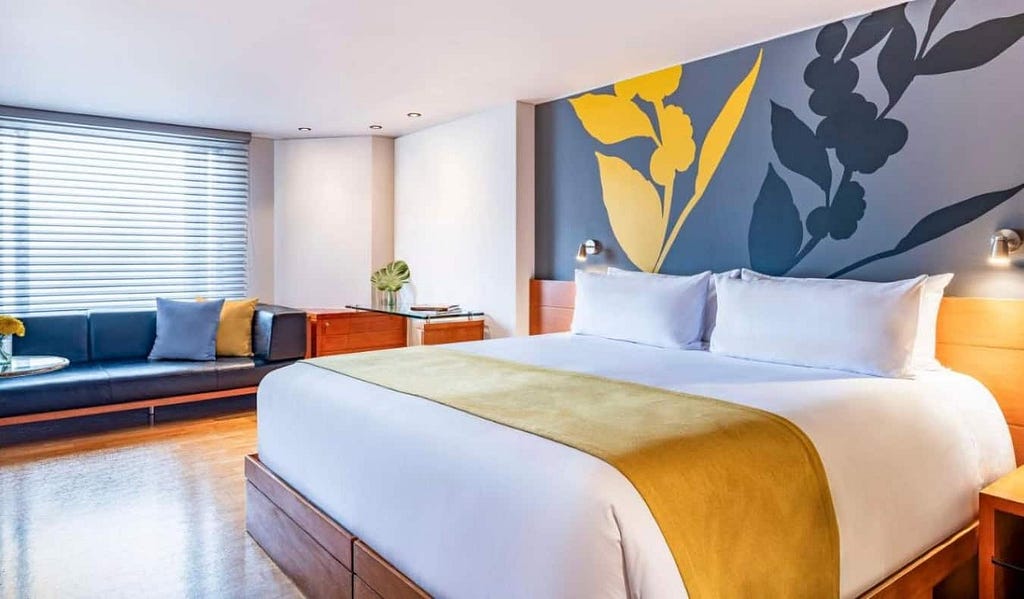 King-sized bed in a guest room with a wall painted with florals, hardwood floors, and a large window bench at Avani Royal Zona T hotel in Bogotá, Colombia