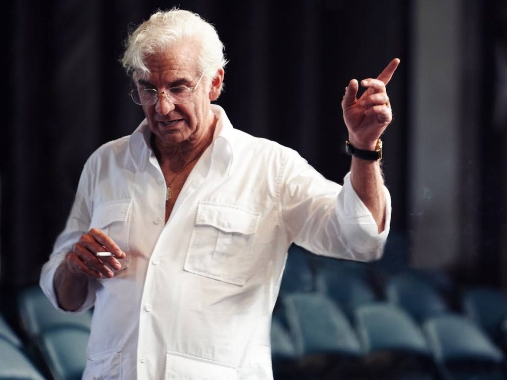 A older man practising conducting and orchestra while smoking (Bradley Cooper playing Leonard Bernstein)