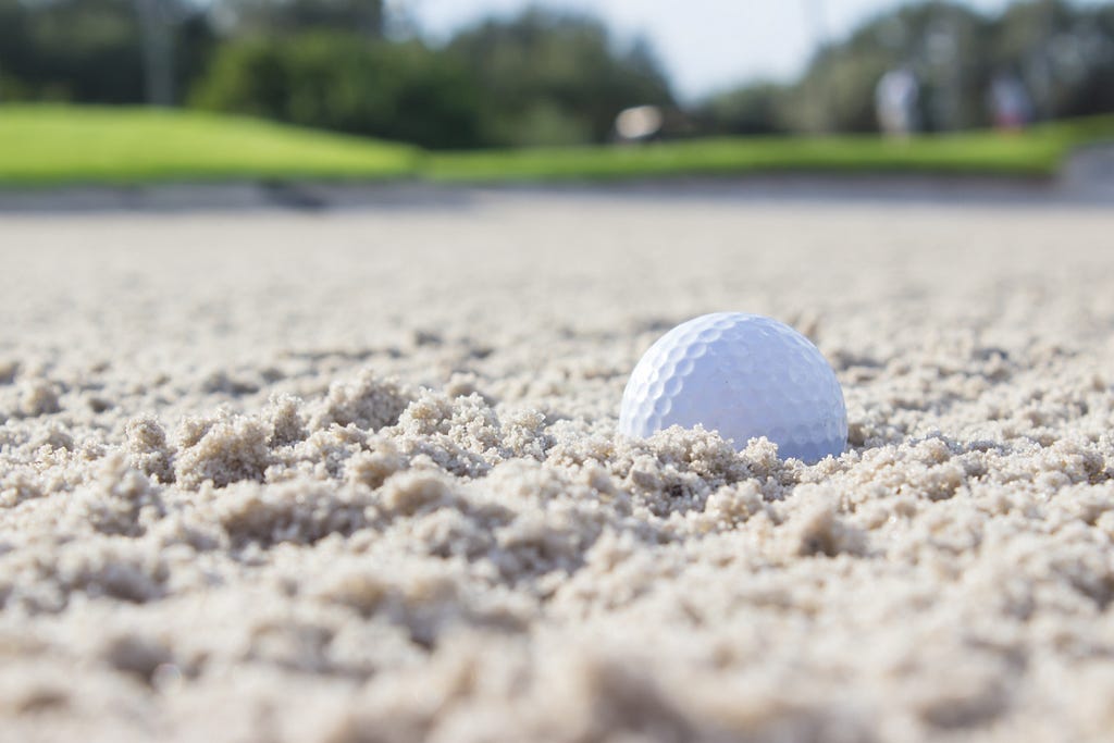 a golf ball plugged in a sand bunker