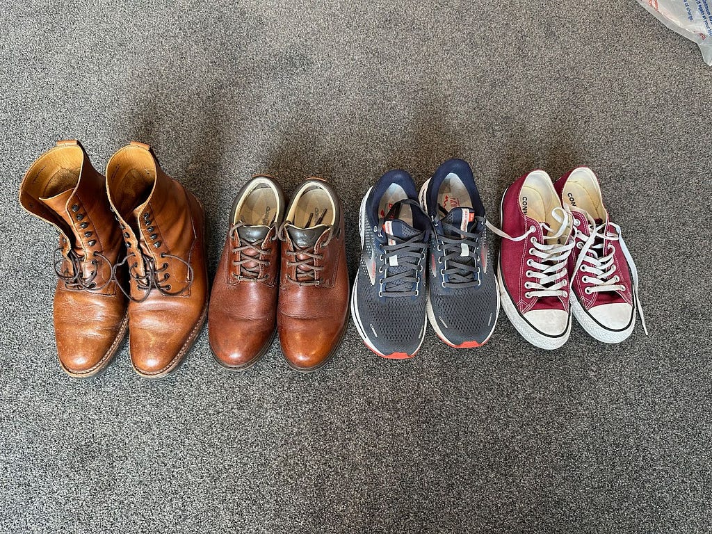 Four pairs of men’s footwear on grey carpet. From left, leather boots, leather shoes, running shoes, Converse shoes.