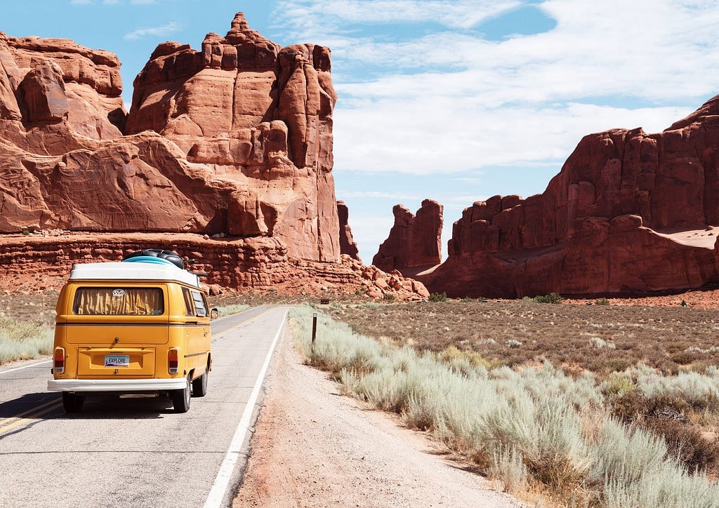 A yellow minivan driving on the road with plateaus up ahead in the distance