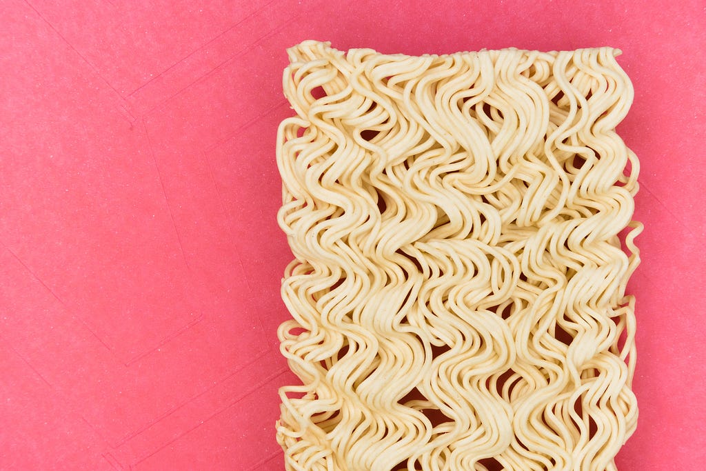 Ramen Noodles uncooked on a pink paper.