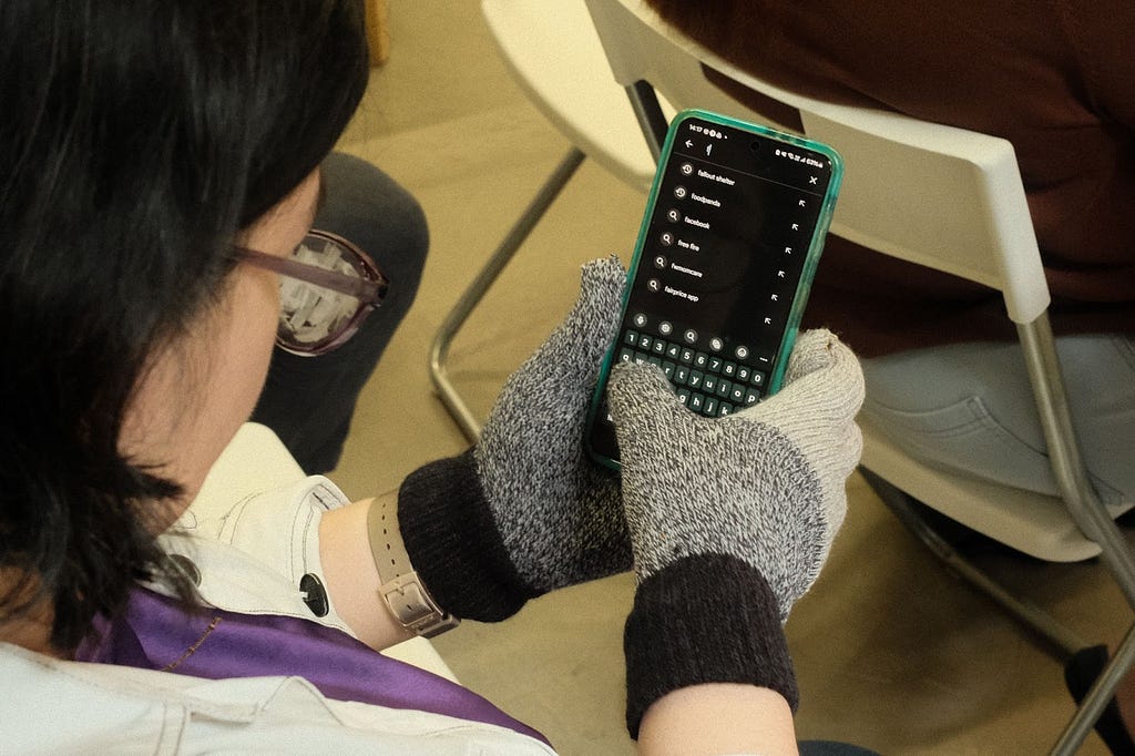 A woman gazing at her smartphone trying to use it while wearing the blurred glasses and hole-poked gloves