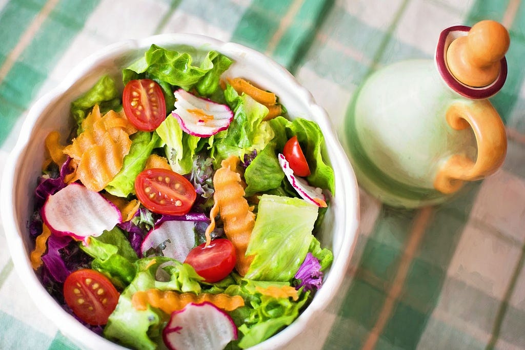 A bowl of salads with salt bottle.