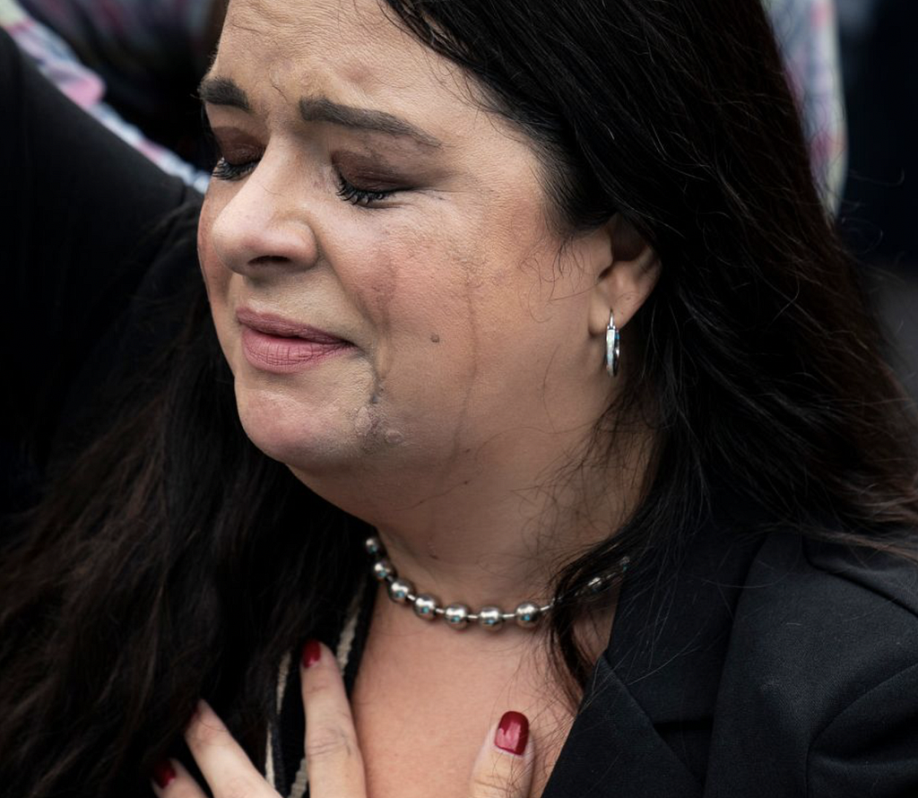 In response to the Dobbs ruling, a white woman with dark brown hair (one of many anti-abortion protestors in from of the Supreme Court on June 24th) closes her eyes and weeps with her left hand over her heart, mascara and eyebrow liner running freely down her face and neck