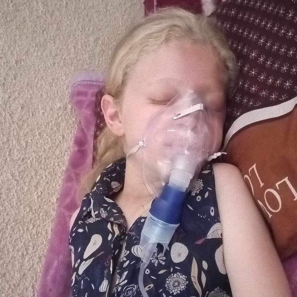 Picture of Judy (8 year old girl with fair skin and blonde hair) with an oxygen mask laying on blankets