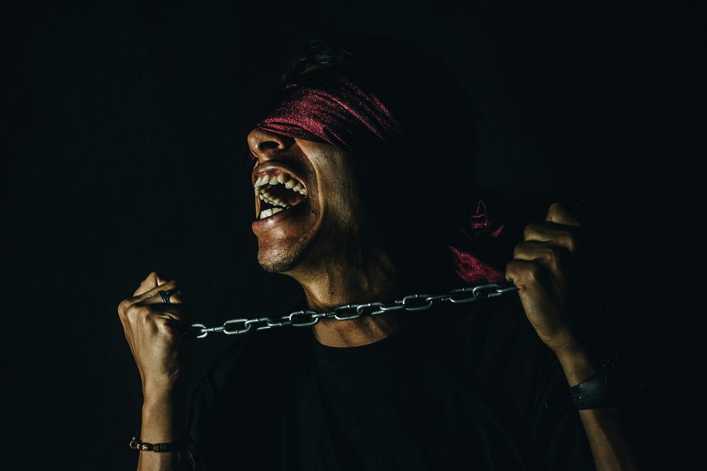 blind-folded man screaming, pulling on a chain with a black background