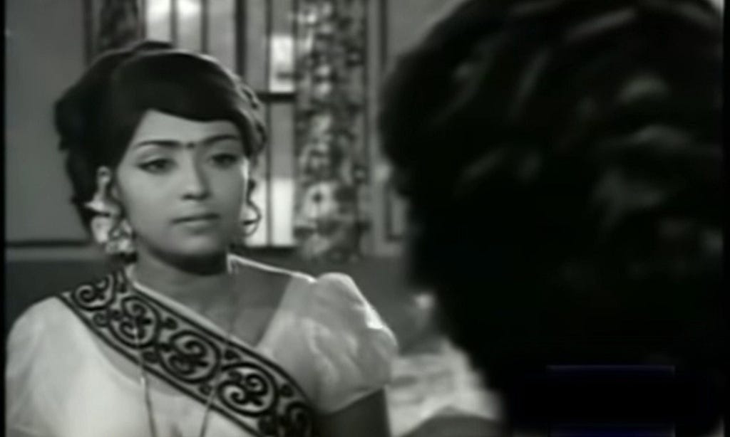 A black and white image shows actress Sujatha as Kavitha. She has on an embroidered sari, big jhumka-like earrings, and a bindi. Her hair is pulled up in an up-do.