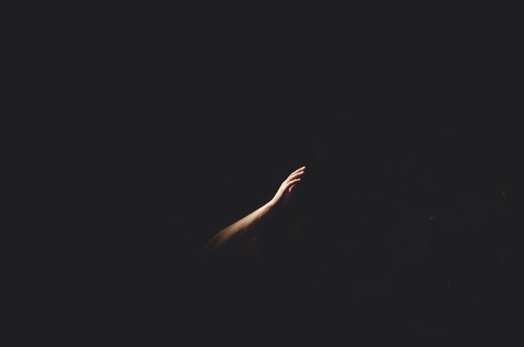 well-lit arm reaching out for help out of a solid black background