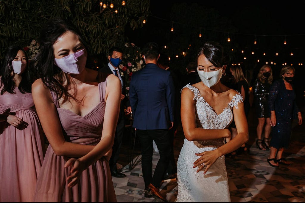 Individuals dance at a wedding while wearing masks.