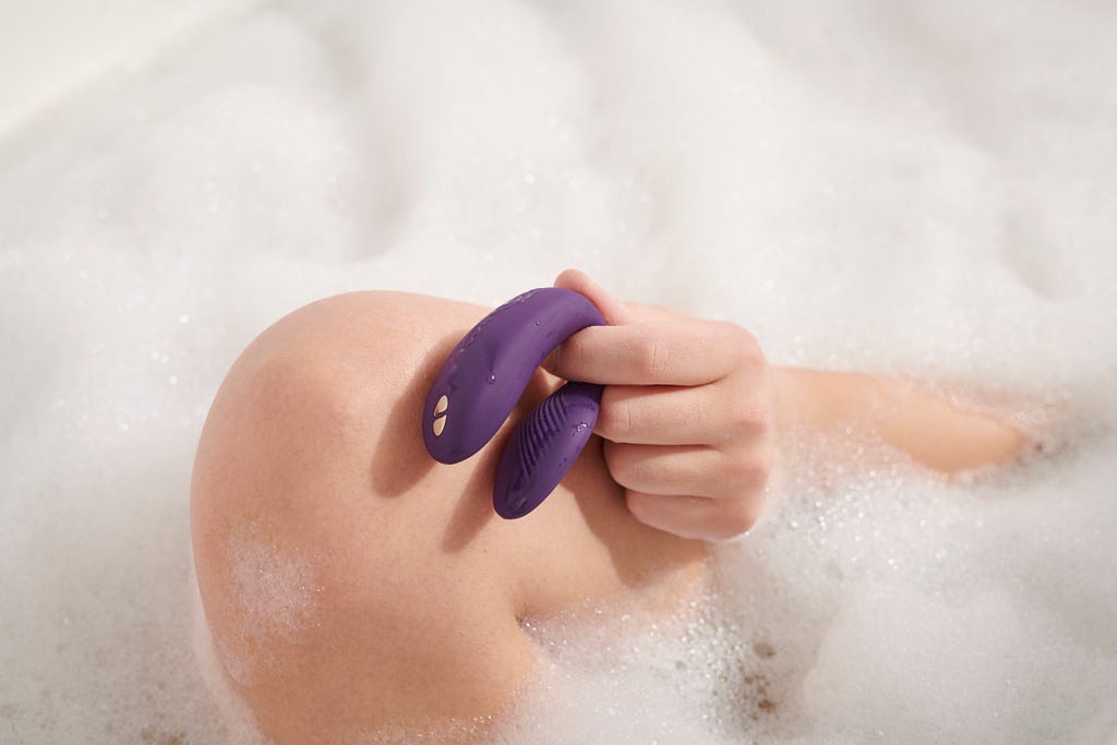 Woman’s hand holding a vibrator in the bath with lots of foam.