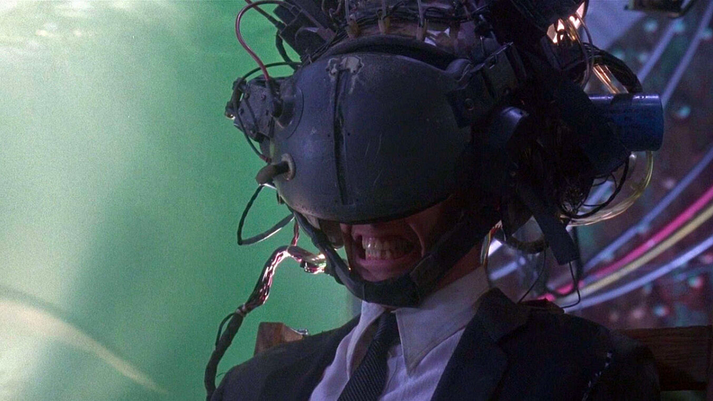 Keanu Reeves in Jonnhy Mneumonic. Most of his face is covered with a strange contraption and he grimaces.