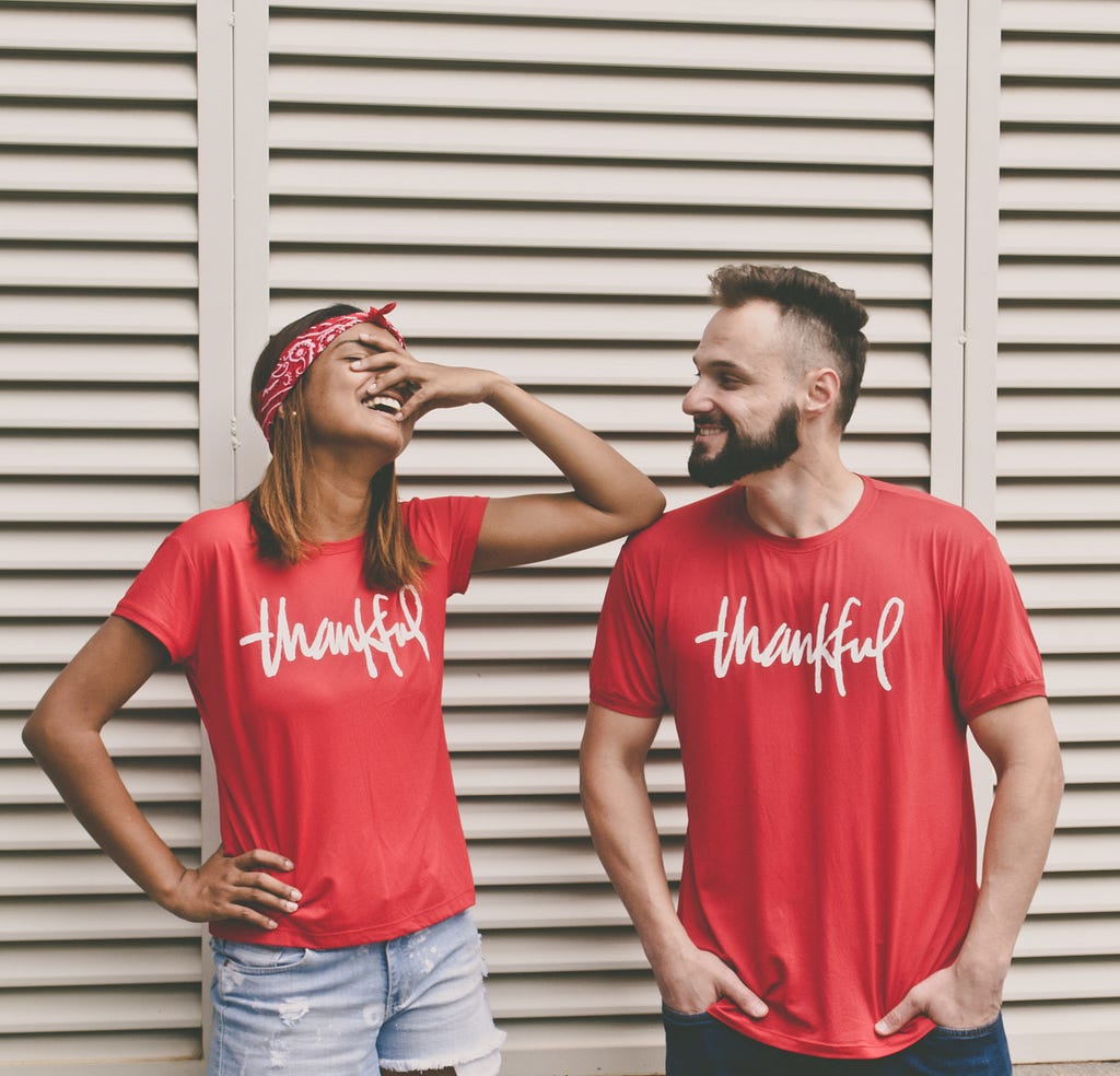 A woman in a red shirt labeled “thankful” grimaces at a man in a similar shirt, perhaps at a joke he cracked.