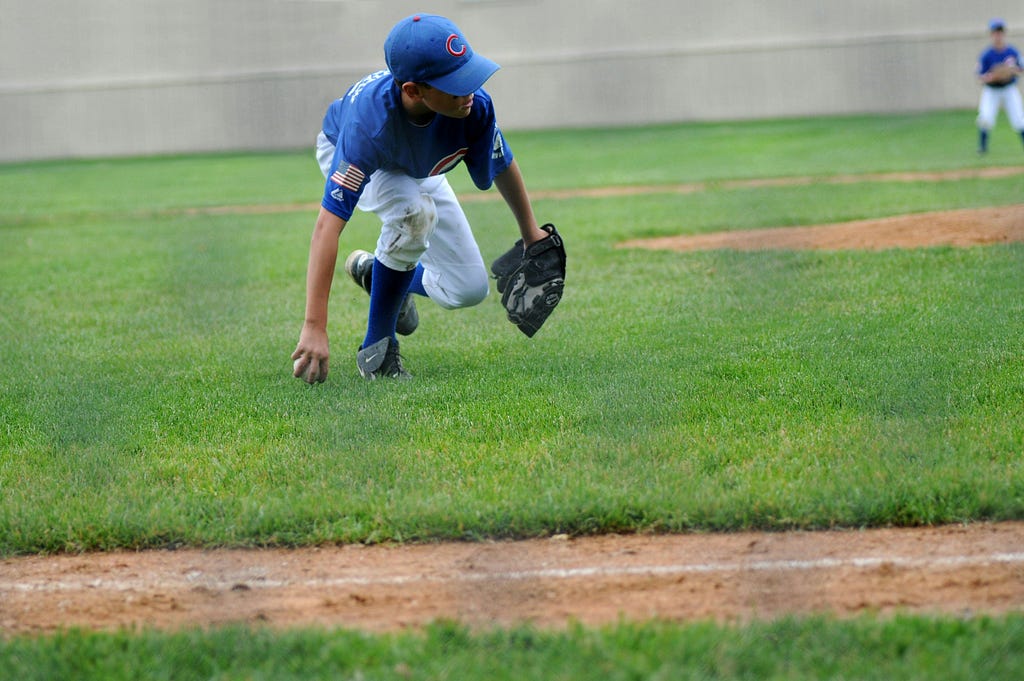 A boy wearing a blue baseball cap and jersey catching a ball.