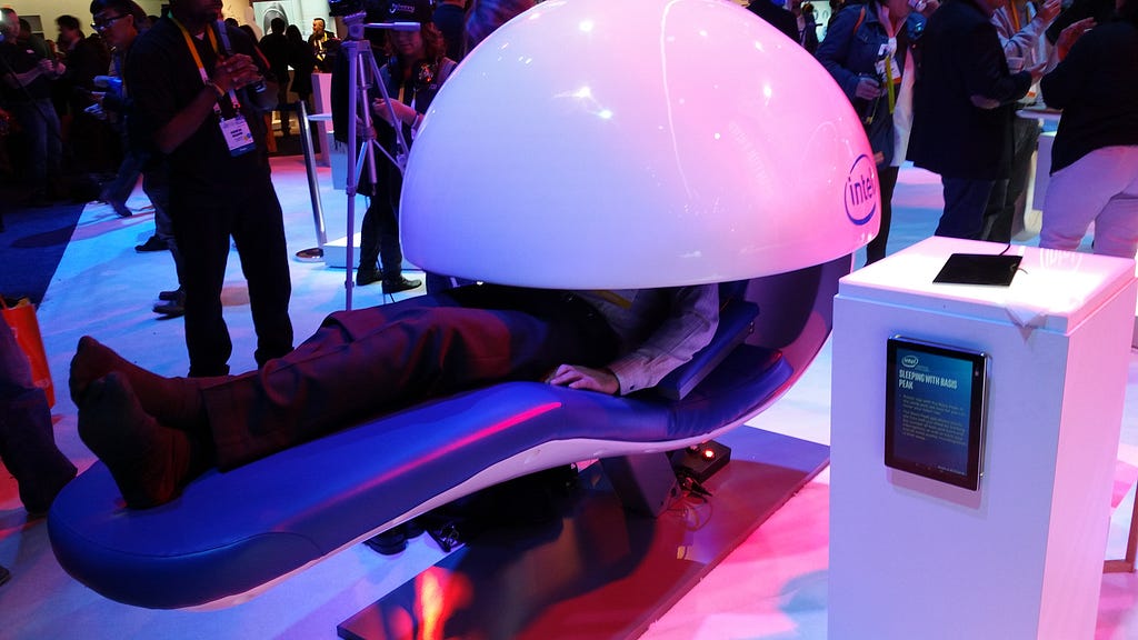 A photograph of a person asleep in a white, futuristic-looking Intel-branded sleep pod at the Consumer Electronics Show in Las Vegas.