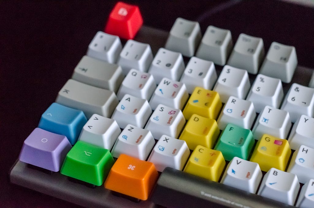 Computer keyboard with colourful keys sitting on a dark background.