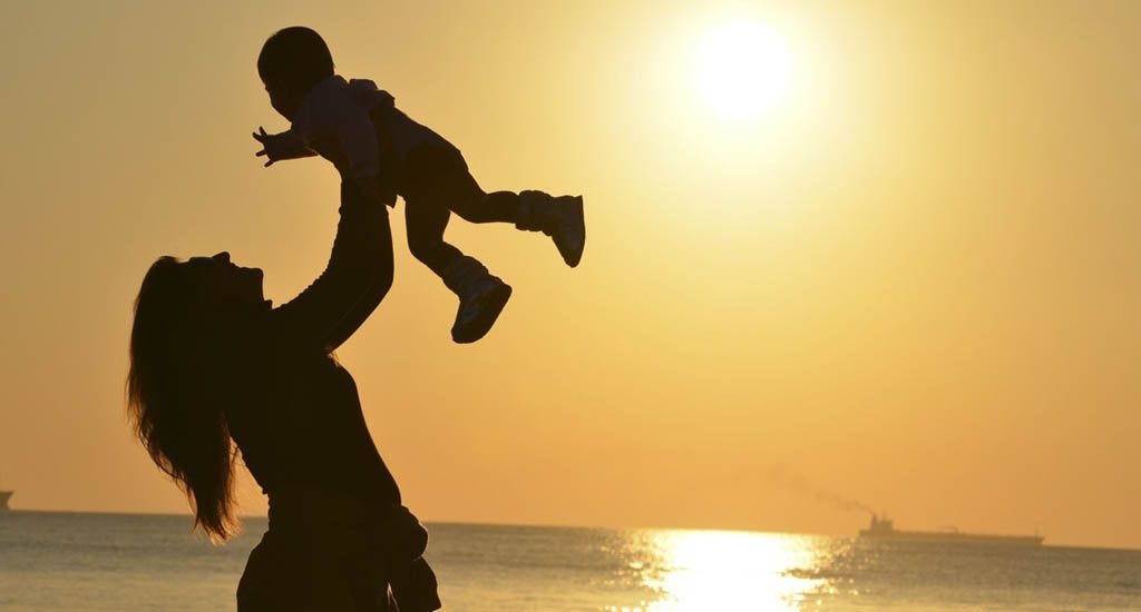 Mother holding child in air against sunset