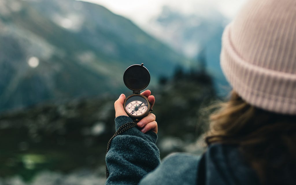 A woman holding a compass against a mountainous background.