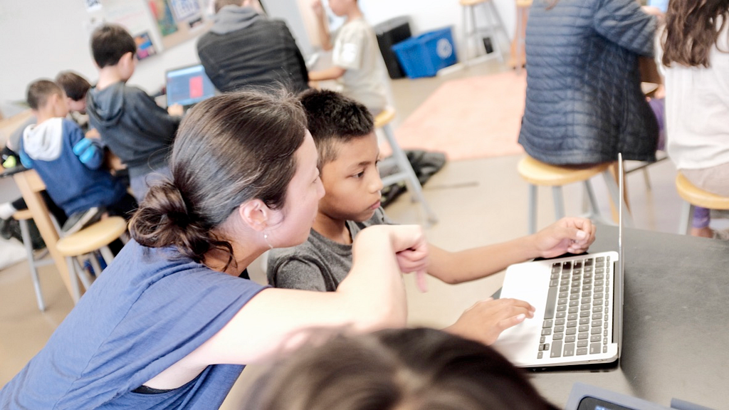 Photograph of Angi working with a student in front of a laptop.