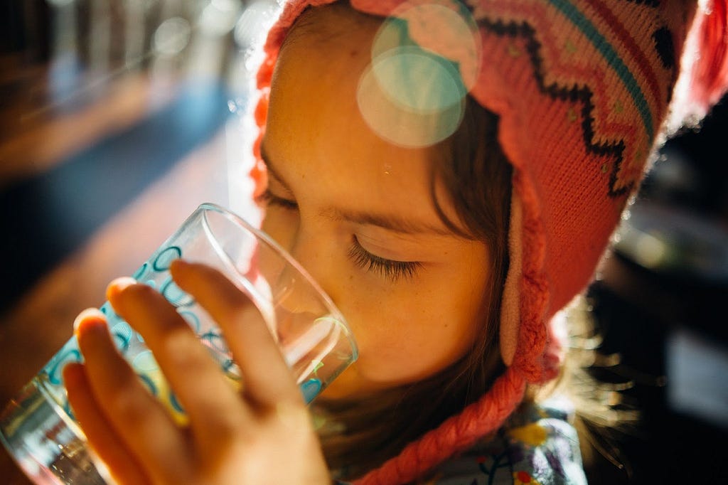 A child drinking water from a transparent glass.