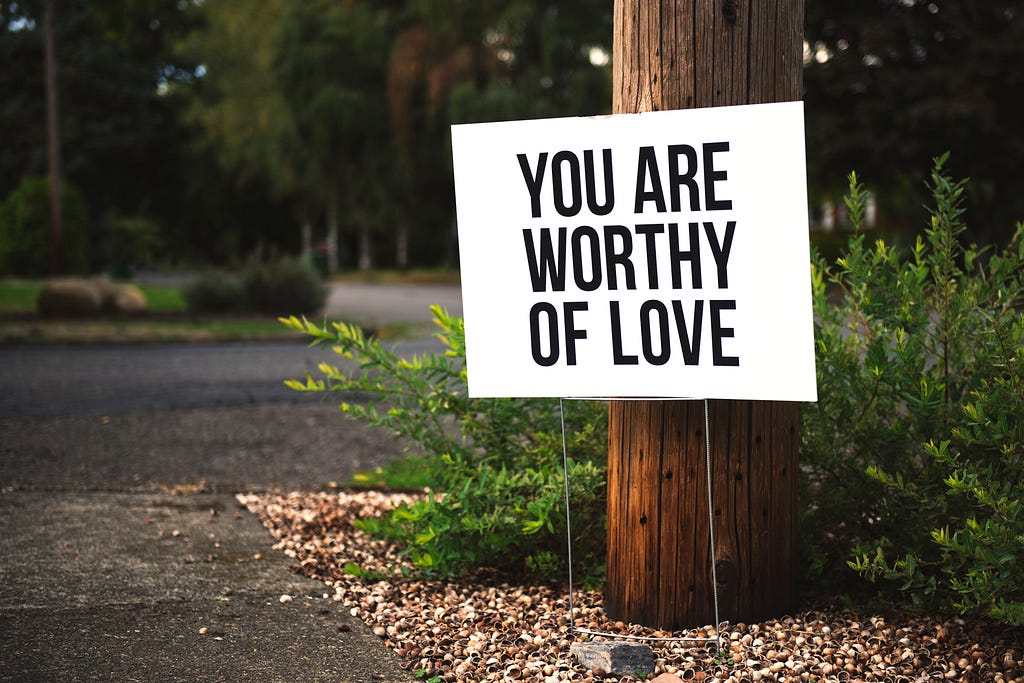 a poster on a tree saying “you are worthy of love”