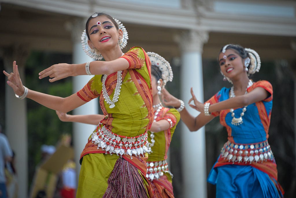 A group of women in saris do a traditional Indian dance.