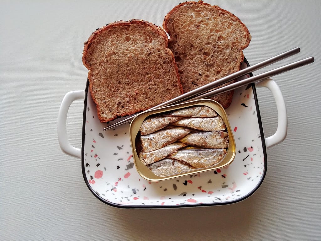 A plate of toast and an opened can of sardines.