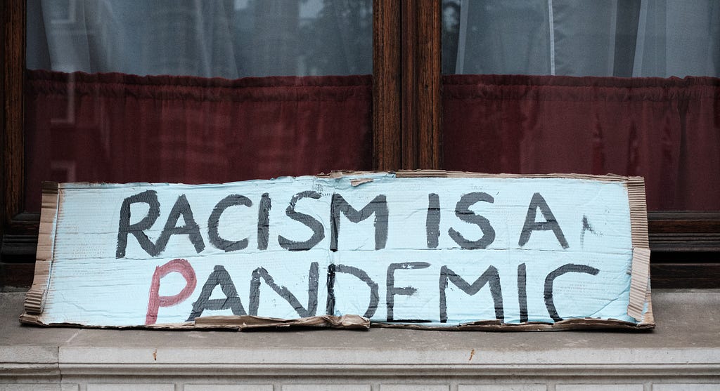 Protest sign sitting in a windowsill stating “Racism is a pandemic”