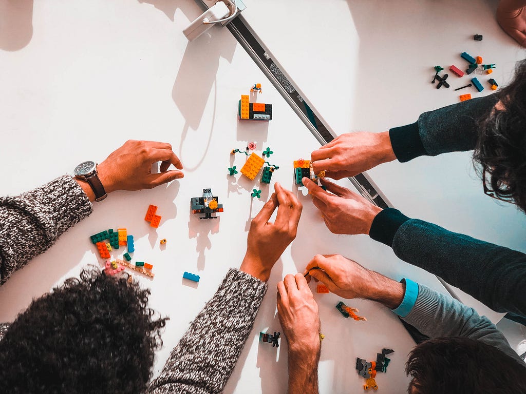 Three people sat at a table are building something with Lego bricks