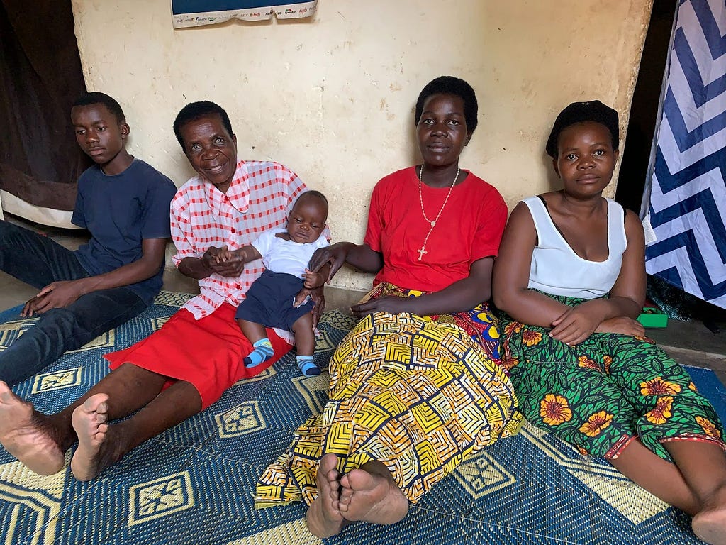 Four adults and a baby sit with their backs against a wall and atop a colorful patterned rug.