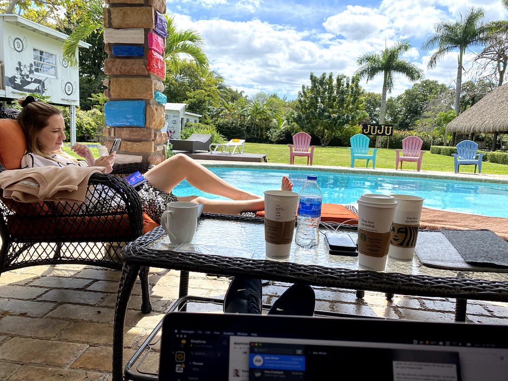 A woman sits on a lounger in front of the pool and next to a table filled with takeout coffee cups.