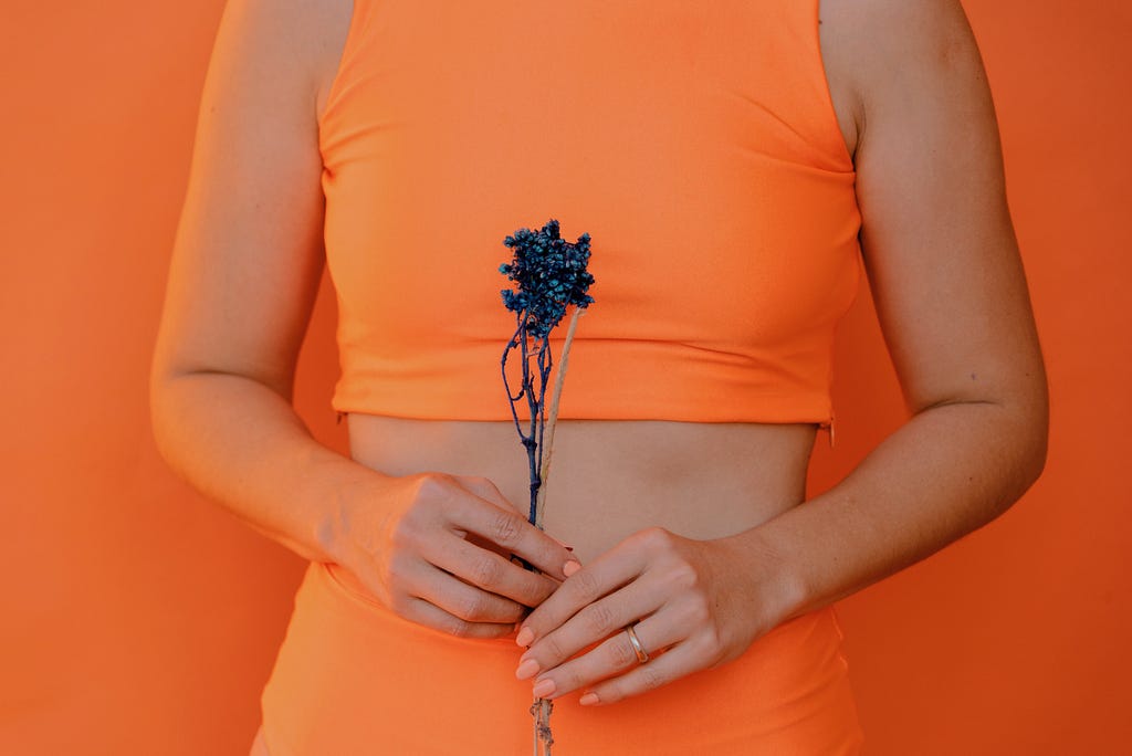 Woman in orange half-top holding a flower in front of her stomach