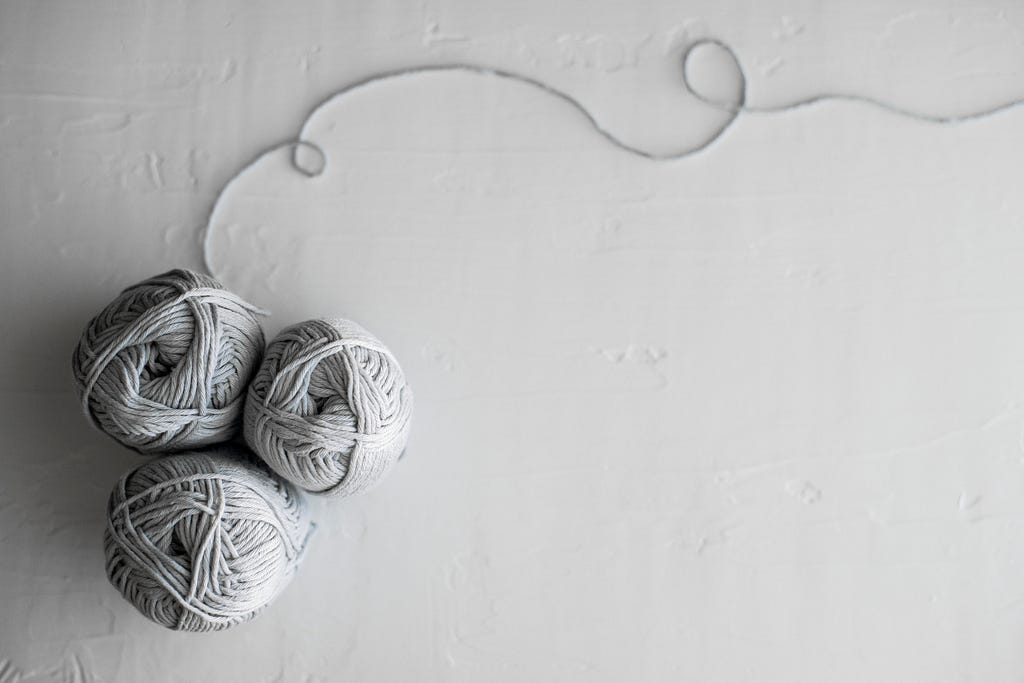 Three balls of yarn group on the left with a trailing string going to the right