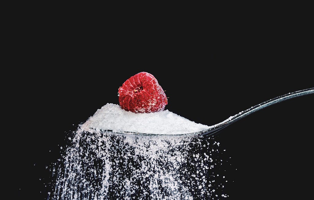 A tablespoon of sugar with a strawberry on top to depict fruits with added sugar.